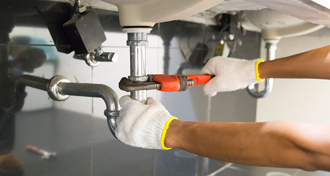 a man wearing white gloves using an adjustable wrench to fix the drainage pipe of a sink