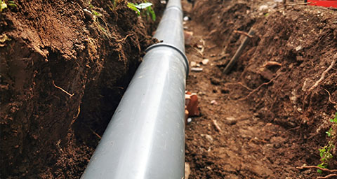 a drainage pipe being installed in the ground in a dug out trench of soil