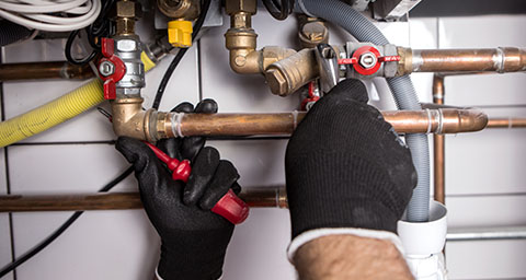 a person with red gloves using a screwdriver to maintain a gas boiler