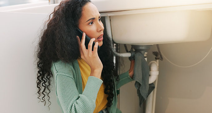 a lady calling a plumber on her phone about a leak from her sink