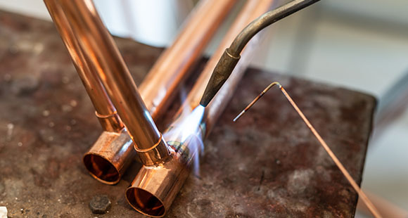 a person welding copper pipes together for central heating piping