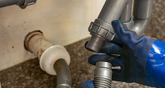 a person wearing thick blue gloves to attach drainage for a washing machine