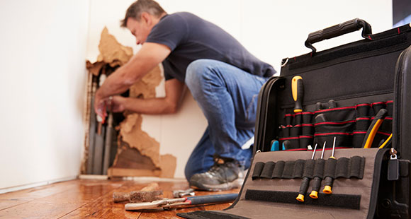 a man fixing some plumbing pipes inside an eroded wall with his toolbox in the foreground