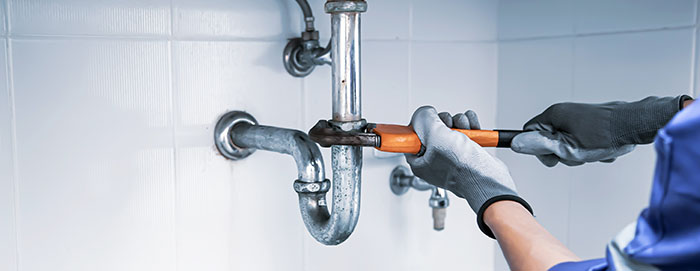 a person with grey gloves using an adjustable wrench to tighten a drainage pipe for a sink